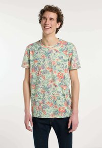 Korte mouwen, lichtgroen t-shirt met een kleurrijk bloemenpatroon met oranje en paarse bloemen, gedragen met donkere spijkerbroek.