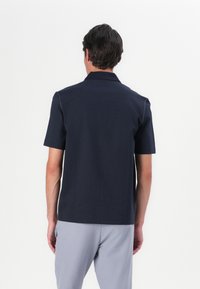 Lühikese varrukaga tumesinine polo särk, millel on lihtne disain, krae, pehme tekstuur ja kontrastne õmblus õlavarre õmblustega.