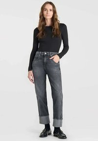 Haut noir à manches longues associé à un jean gris taille haute et ample, avec revers aux chevilles et mocassins noirs élégants. Design minimaliste.