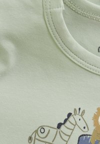 Ljusgrön bomullströja med rundad halsringning, med ett illustrativt mönster av djur, inklusive en zebra och ett lejon, i mörka och beige toner.