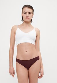 Bralet alb scurt cu bretele subțiri, asortat cu slipuri de bikini burgundy. Material moale, design fără cusături și stil minimalist.