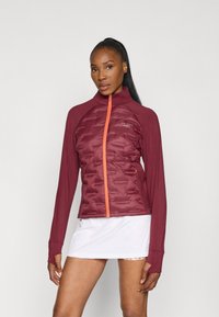 Giacca bordeaux con textura trapuntata, zip arancione, maniche lunghe e design aderente. La giacca presenta un colletto alto per un comfort maggiore.