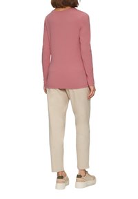 Langärmliges, pinkes Oberteil mit rundem Ausschnitt, kombiniert mit hellbeigen, taillierten Hosen und beigen Sneakers mit strukturierten Sohlen und Akzentdetails.