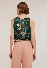 Bezramienna zielona bluzka w kwiatowy wzór w odcieniach różu i brązu; zestawiona z jasnoróżowymi spodniami z tylnymi kieszeniami i teksturowanym paskiem.