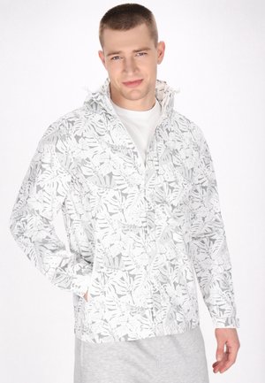 Hvid zip-up jakke med grå bladmønstre, der har hætte, lange ærmer og sidelommer. Båret over en simpel hvid skjorte.