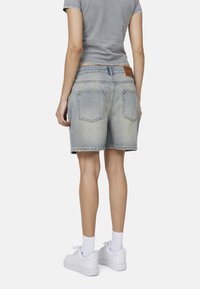 Jasnoniebieskie szorty dżinsowe o luźnym kroju, pięciopocketowy design i postrzępiony brzeg. Noszone z białymi trampkami i skarpetkami do kostek.