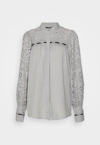 Blouse à manches longues gris clair avec détails en dentelle à œillets sur les manches et le yoke, col à boutons et patte de boutonnage avant dissimulée.