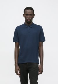 Polo-shirt à manches courtes bleu marine en coton, avec un col classique, une patte de boutonnage à trois boutons et un détail de logo minimal sur la poitrine.