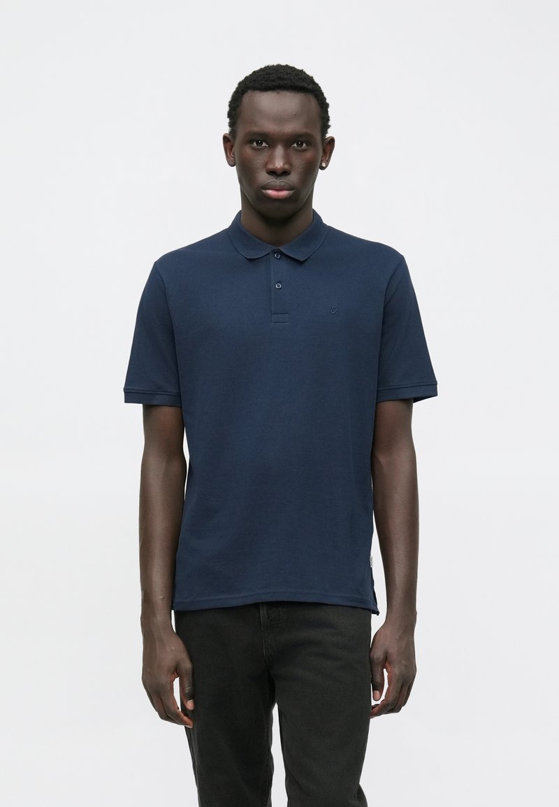 Polo-shirt à manches courtes bleu marine en coton, avec un col classique, une patte de boutonnage à trois boutons et un détail de logo minimal sur la poitrine.