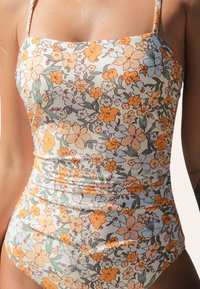 Bloemen een-delige swimsuit met een vierkante halslijn. Heeft oranje en pastelblauwe bloemen op een lichte achtergrond. Gemaakt van een gladde, rekbare stof.