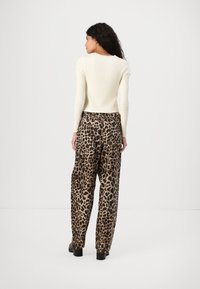 Ribbed white long-sleeve sweater paired with loose-fitting tan leopard print pants. Smooth texture with distinctive animal pattern.