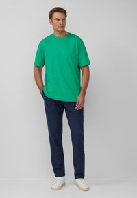 Zielona, krótka koszulka z lekkiego materiału. Połączona z ciemnogranatowymi spodniami i białymi sneakersami. Prosty design, bez widocznych wzorów.