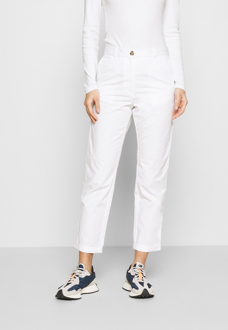Pantalones de algodón blancos con corte recto, cintura de altura media, cierre de botón en la parte delantera y dos bolsillos laterales. Llevados con zapatillas de deporte con estampado.