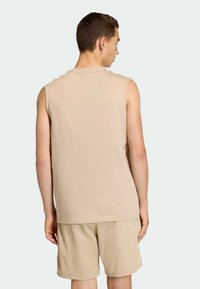 Bež majica bez rukava od mekane tkanine, s jednostavnim dizajnom. Uparen s teksturiranim kratkim hlačama svijetlo bež boje, prikazano sa stražnje strane.