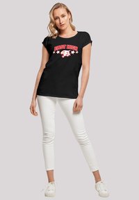Sort bomulds t-shirt med "EAST HIGH" i rødt, med et hvidt ørne-logo og fem hvide stjerner. Matchet med hvide slim-fit jeans og sneakers.
