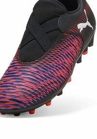 Scarpa da calcio nera con superficie texturizzata caratterizzata da audaci motivi a zigzag rossi e viola, accentuata da un elastico nero e tacchetti rossi.