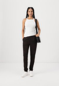 White tank top with halter neck design, paired with black pants featuring a dark brown zebra pattern. White sneakers and a small black bag.