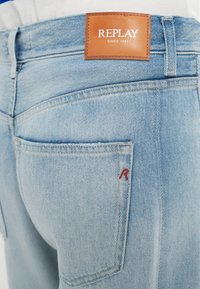Ανοιχτό μπλε τζιν παντελόνι με δερμάτινο ταμπελάκι "REPLAY" στη μέση. Διαθέτει ένα μικρό κόκκινο 'R' ραμμένο στην πίσω τσέπη.