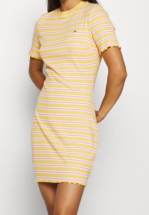 Mujer con un vestido ajustado amarillo con rayas horizontales rosas y blancas y bordes con volantes en las mangas y el dobladillo.