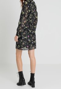 Schwarzes Blumenkleid aus durchsichtiger Stoff, mit langen Ärmeln und elastischem Bund. Getragen mit schwarzen Schnürstiefeln bis zu den Knöcheln.