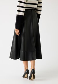 Gonna di pelle nera con un design svasato e un orlo sopra la caviglia, abbinata a eleganti scarpe con tacco nero.