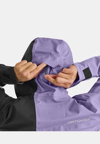 Purple and black outdoor jacket with a flexible hood. Features an adjustable drawstring, velcro cuffs, and sleek texture for wind protection.