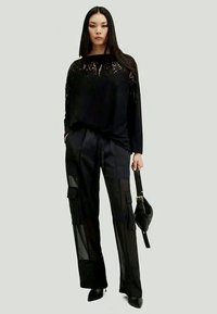 Top preto de manga longa com detalhes em renda, combinado com calças cargo pretas com painéis transparentes e múltiplos bolsos. Inclui uma bolsa preta.