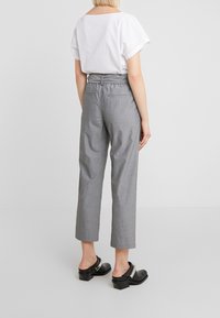 Grå, löst sittande byxor med hög midja och sidofickor, i kombination med en vit t-shirt med kort ärm och svarta träskor.