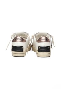 Białe sneakersy z metaliczno-różowymi akcentami, czarnym teksturowanym detalem na pięcie i jasnobeżową podeszwą. Minimalistyczny design z wiązaniem.