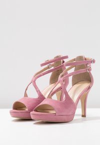 Sandalias de tacón alto de ante rosa con punta abierta, múltiples tiras entrelazadas y una base de plataforma. Forro interior suave y tacón delgado.
