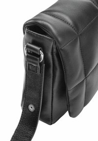 Czarna skórzana torba z pikowanym wzorem, z metalowymi akcentami oraz teksturowanym paskiem przymocowanym srebrnymi klamrami.