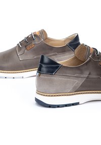 Chaussures hybrides marron en cuir et en daim, avec un design perforé, des accents de talon noirs contrastants et une semelle blanche avec des détails bleus.
