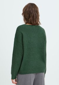 Maglione verde lavorato a maglia con una trama a costine, vestibilità rilassata e spalle scese. Presenta maniche lunghe e un ampio scollo.