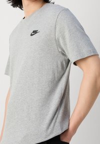 Szara koszulka z krótkim rękawem z bawełny, z czarnym logo Nike na piersi, okrągłym dekoltem i gładką teksturą.