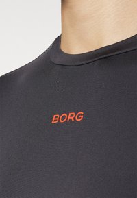 Crna sportska majica kratkih rukava, s glatkom teksturom i okruglim izrezom. "BORG" je istaknuto prikazan u crvenoj boji.