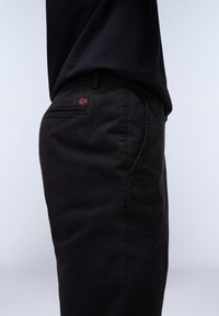 Pantaloni in cotone neri con vestibilità rilassata, caratterizzati da una piccola etichetta con la bandiera norvegese rossa e bianca sulla tasca posteriore e una leggera trama.