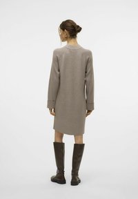 Strickkleid in Hellbraun, mit lässiger Passform, langen Ärmeln, gerippten Akzenten am Kragen und an den Bündchen, kombiniert mit hohen braunen Stiefeln.