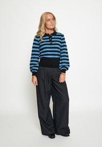 Plava i crna prugasta polo majica dugih rukava s tri dugmeta, u paru s labavim, crno prugastim hlačama i crnim cipelama.