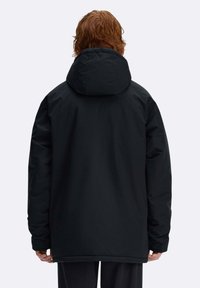 Giacca nera con cappuccio dal taglio ampio, caratterizzata da una texture liscia, maniche lunghe e tasche lungo le cuciture laterali. Nessuna ferramenta o motivo visibile.