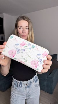 Portfel w kwiaty z białym tłem i różowo-niebieskimi wzorami, gładka tekstura, zamek błyskawiczny oraz złote akcenty.