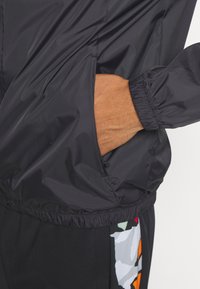 Schwarze leichte Jacke mit einer Tasche, elastischen Bündchen und einem cinched Saum. Das Design enthält ein farbenfrohes, gemustertes Akzent.
