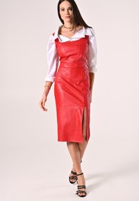 Rotes Leder-Midi-Kleid mit Schulterträgern, taillierte Silhouette, dezenter Schlitz vorne, kombiniert mit einem weißen Hemd mit Knöpfen und schwarzen Riemchen-Heels.