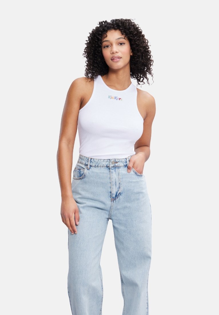 Camiseta sin mangas blanca de canalé con el texto "Kook" en letras multicolores, combinada con unos vaqueros de denim claros de cintura alta.