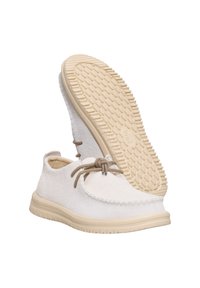 Scarpe in suede bianco con una suola in gomma beige, caratterizzate da una punta tonda, dettagli cuciti e un fiocco in pizzo marrone davanti.