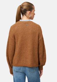 Pull en maille marron à coupe ample avec des manches dramatiques ; fabriqué en matériau doux et texturé, avec une petite étiquette à l'arrière.