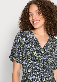 Vestido floral envolvente com mangas curtas, apresentando um fundo preto, pequenas flores azuis e amarelas, e um decote em V. Tecido leve.