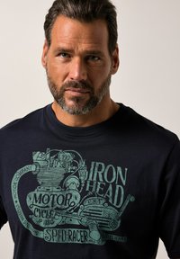Námořnická modrá bavlněná tričko s grafikou vintage motocyklového motoru v zelené barvě, se stylizovaným textem "Iron Head" a "Motor Company."