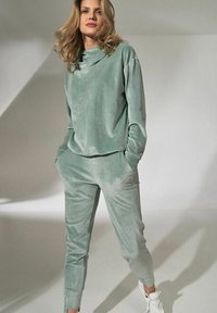 Lichtgroen velours trainingspak met een ontspannen pasvorm, hoge kraag en taps toelopende broek. Soepele textuur met zijzakken en elastische manchetten.