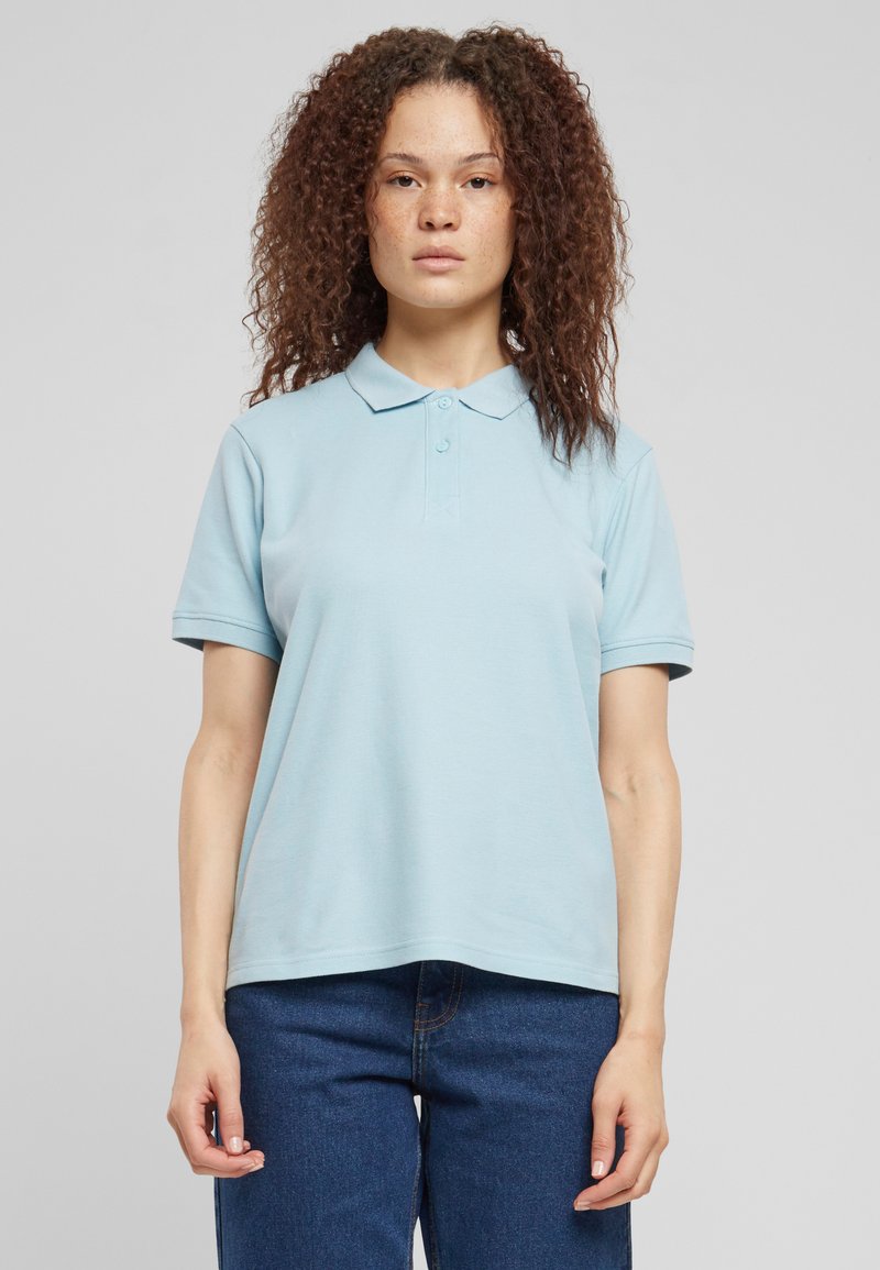 Lyseblå polo skjorte laget av myk stoff med klassisk krage, korte ermer og knappestolpe med to knapper; brukt med mørkeblå jeans.