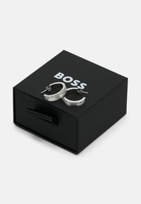 Sølv hoops øredobber med en klar rhinestone-bånd, vist i en svart eske med et båndhåndtak og en fremtredende "BOSS"-logo.